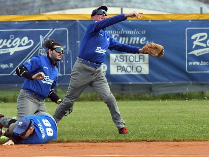 in un campo di baseball un uomo con deficit visivo lancia la palla sonora. Nella mano sinistra porta il guantone e sugli occhi ha una mascherina che scherma la luce. Dietro di lui ci sono altri due giocatori con la stessa maschera sul volto: uno scivolato a terra e l'altro in ginocchio che osserva la traiettoria della palla.