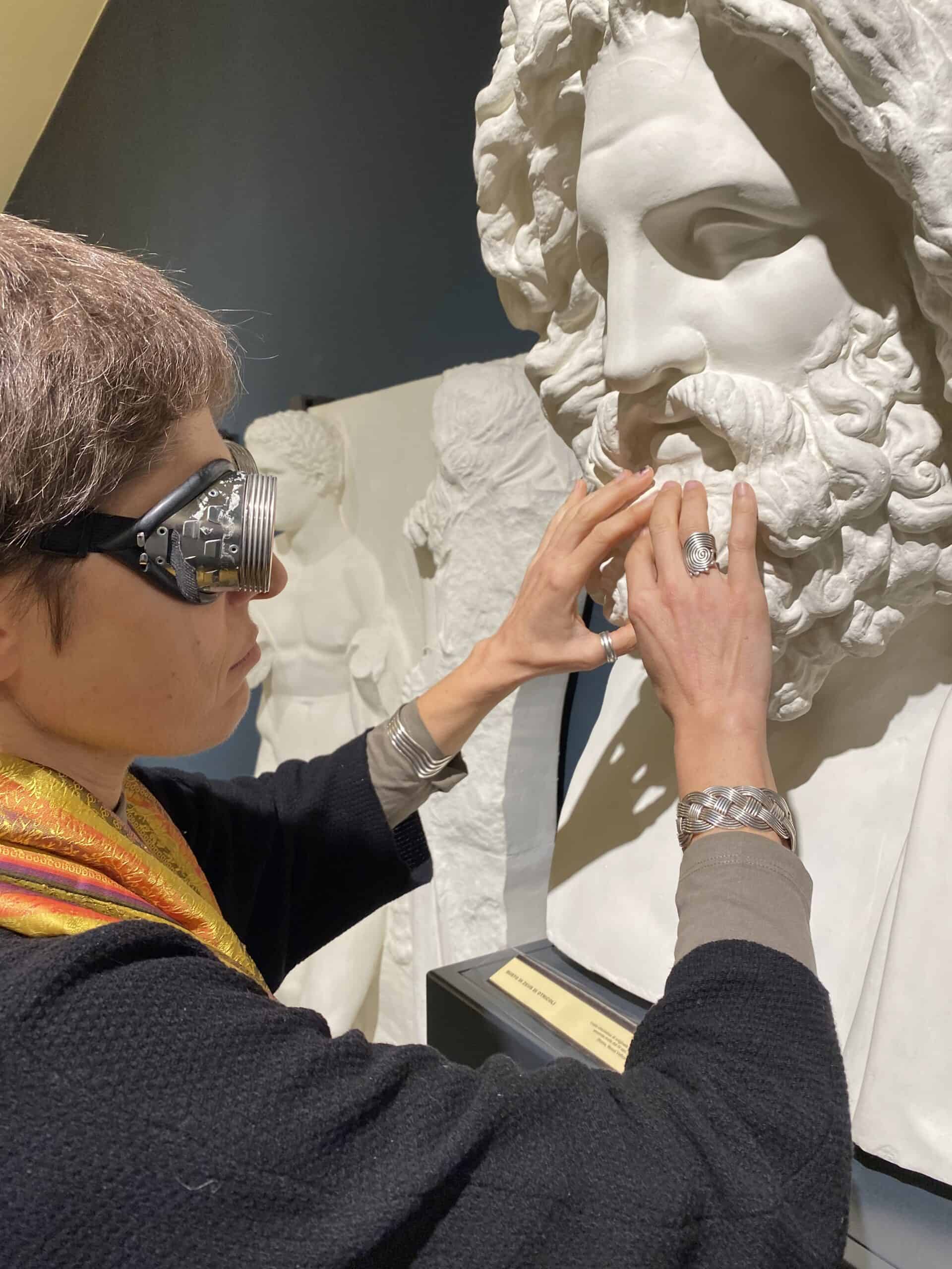 una donna bendata tocca con le mani il volto ricostruito di un busto antico presente all'interno del Museo di archeologia e d'arte dell'Unipd