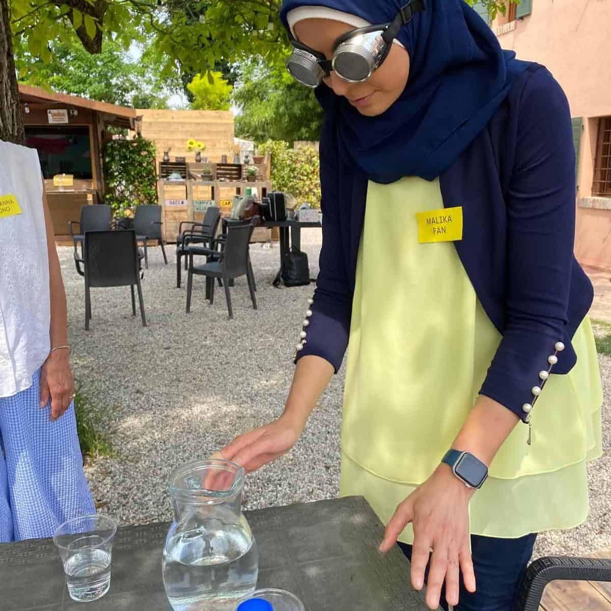 Formazione esperienziale del progetto sensoriAbile anch'io al chiosco del parco dei Girasoli a Padova. Una ragazza con occhiali che simulano l'ipovisione cerca di versare da una brocca trasparente dell'acqua su un bicchiere trasparente.