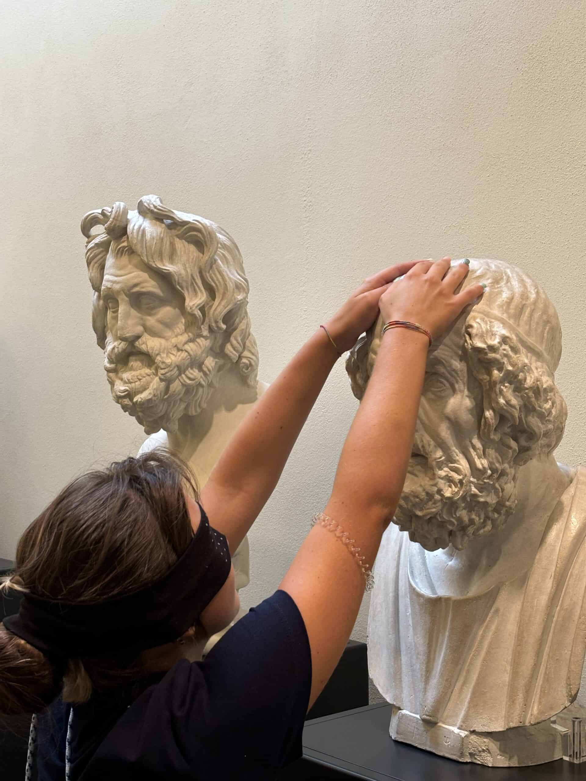 Una ragazza bendata esplora con le mani un busto antico all'interno del Museo di Scienze Archeologiche.