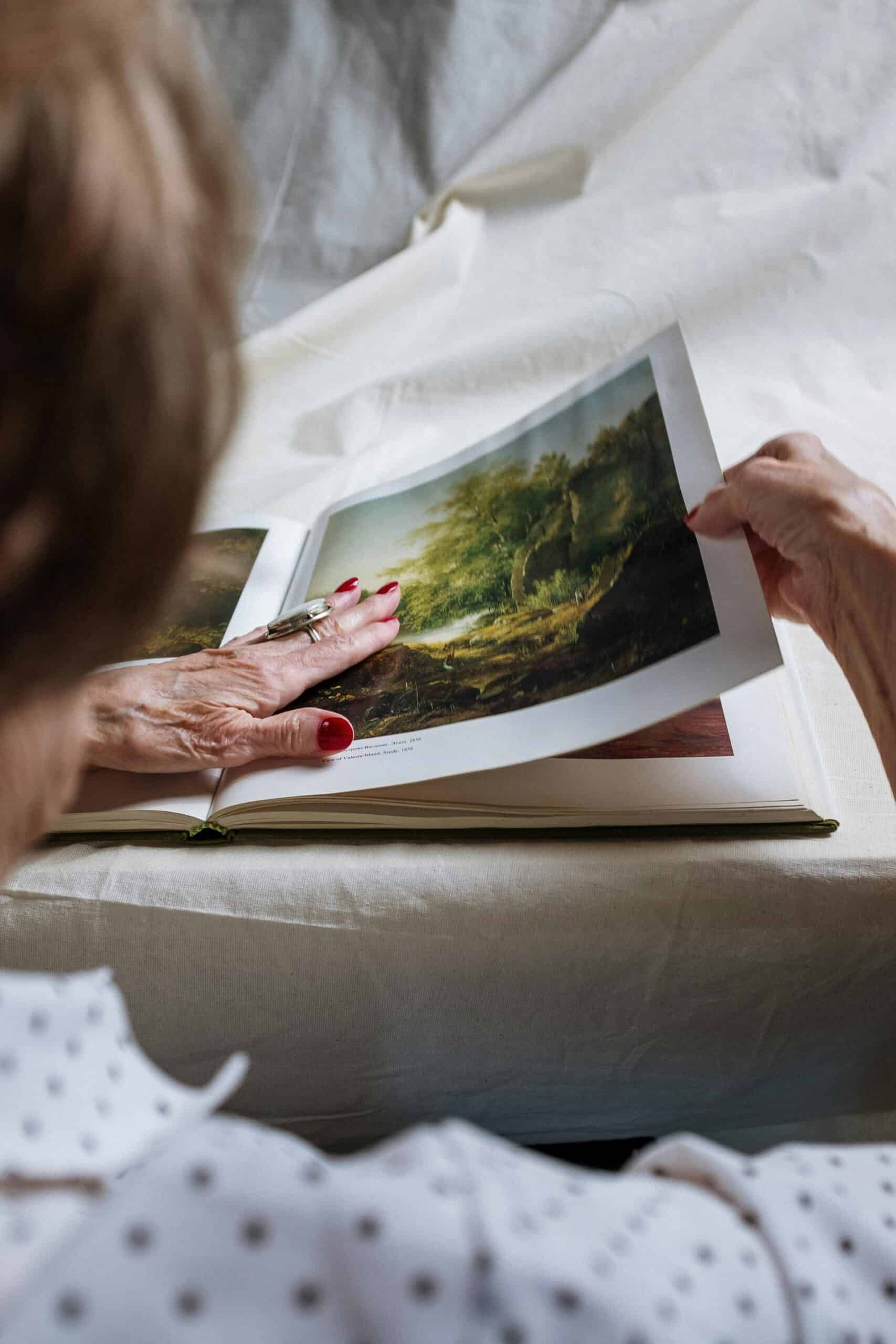 le mani di un'anziana toccano l'immagine di un paesaggio stampata su un libro.