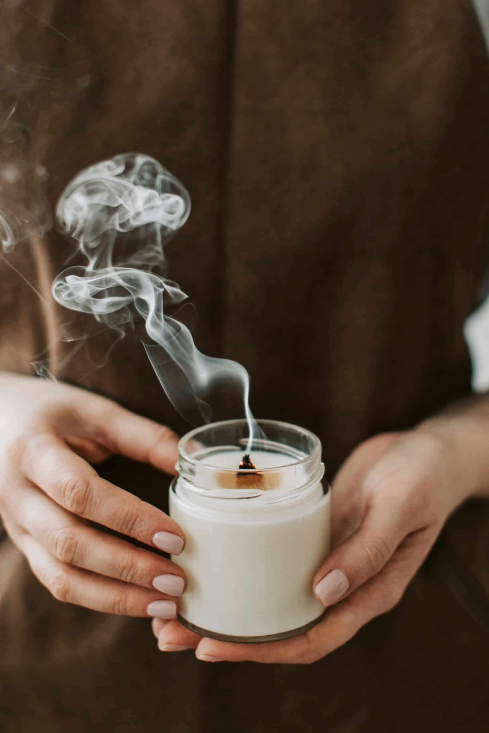 le mani di una donna tengono una candela appena spenta all'interno di un vaso di vetro. Del fumo si alza dallo stoppino.